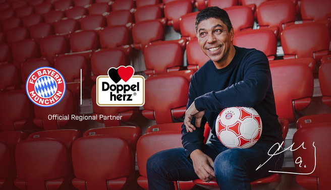 Un homme souriant assis sur des sièges rouges tient un ballon de football. À côté de lui, les logos du FC Bayern Munich et de Doppelherz sont visibles, avec la mention "Partenaire régional officiel". L'image évoque le partenariat dans le cadre du sport.